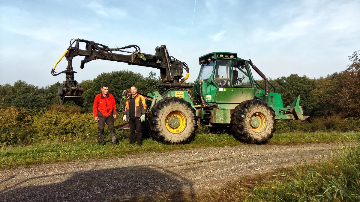 Bild für die Leistung "Verkehrssicherungsmaßnahmen". Grüner Traktor. Davor stehend 2 Personen.